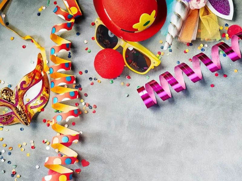 Karneval am Donnerstag: Goldene Maske, bunte Luftschlangen, rote Clownsnase und Konfetti laden zum Feiern ein.