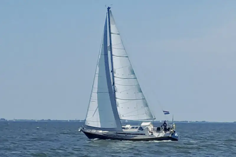 Voilier blanc et bleu naviguant sur une mer calme sous un ciel clair. Les voiles sont gonflées par le vent. Les premiers 375 avis sur ce type de bateau sont positifs.