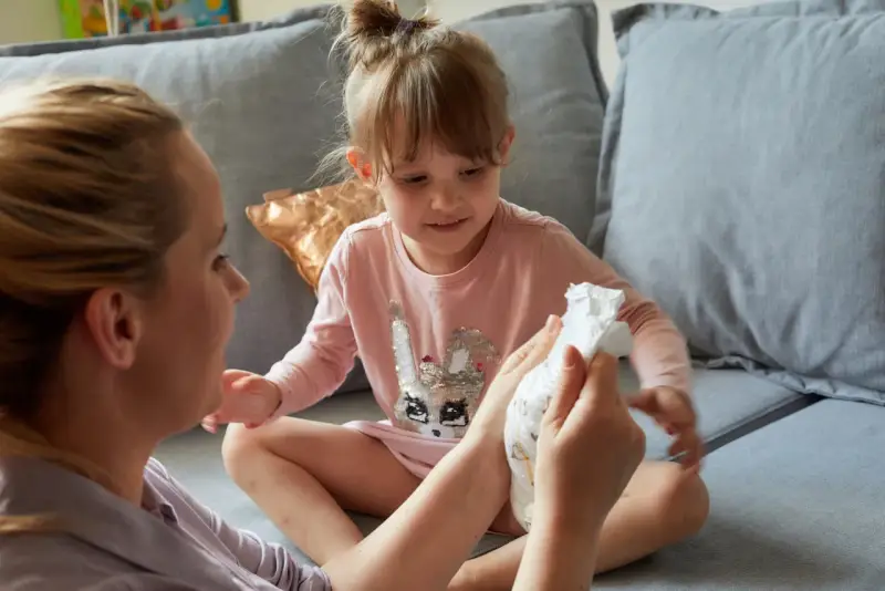 Mama pokazuje córce pieluchę, symbolizując etap, kiedy dziecko przestaje nosić pieluchy.
