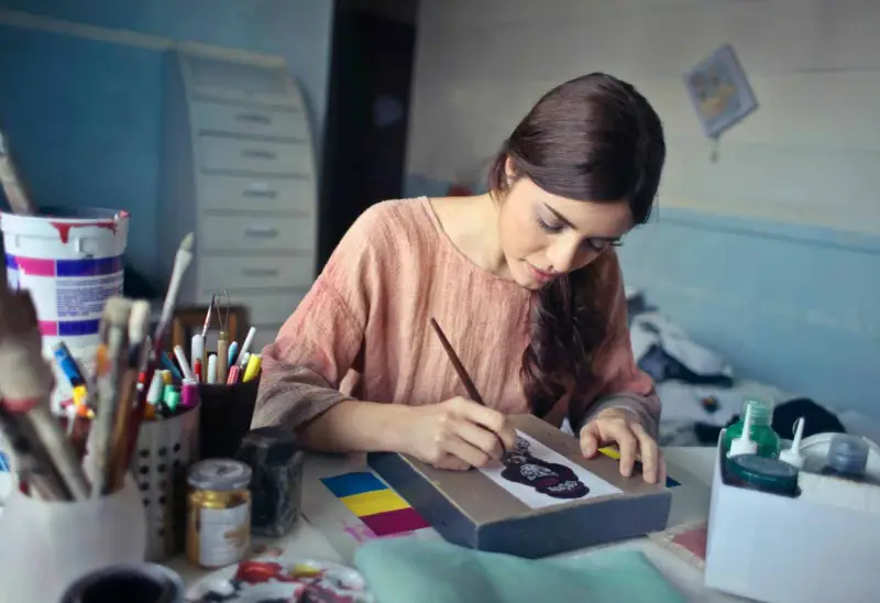 Une jeune femme se déclare artiste libre, concentrée sur sa toile, entourée de pinceaux et de peintures.
