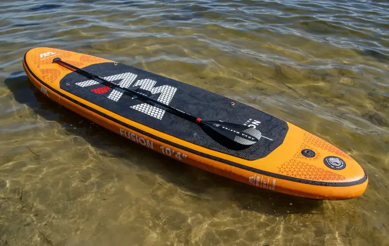 Pomarańczowy aquamarina sup z wiosłem leży na płytkiej, przejrzystej wodzie.