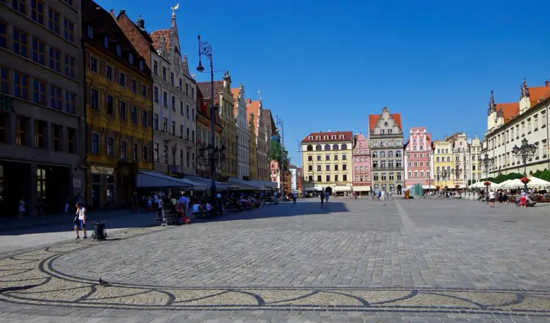 Kolorowy Rynek we Wrocławiu, idealne miejsce na jednodniowe wycieczki z Wrocławia. Ludzie spacerują, siedzą w kawiarniach, ciesząc się słońcem.