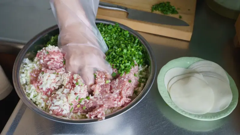 Mieszanie mielonego mięsa, kapusty i szczypiorku do pierożków gyoza. Przepis na pyszne domowe pierożki.