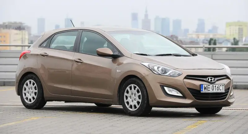 Brązowy Hyundai i30 1.6 benzyna na parkingu z widokiem na miasto w tle.