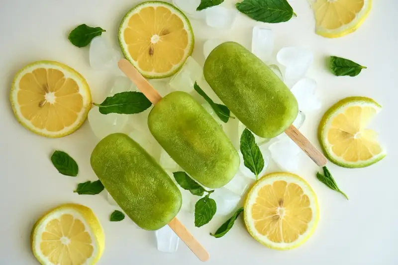 Trois bâtonnets glacés verts, comme une coupe colonel rafraîchissante, entourés de citrons, de menthe et de glaçons.