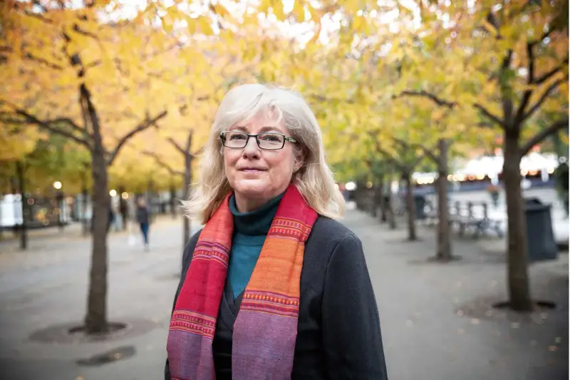 Kvinna med glasögon och färgglad scarf i höstpark. Hon verkar inte ha ont i leder brist på energi, utan njuter av den vackra naturen.