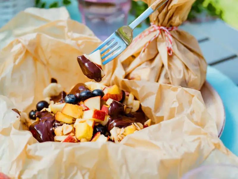 Fruchtiger Nachtisch vom Grill: Apfelstücke, Blaubeeren und Bananen mit Schokoladensauce, serviert in Papier.
