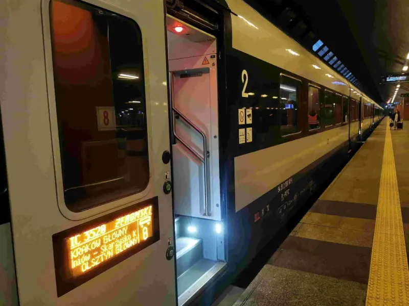 Drzwi otwartego pociągu na peronie, widoczny wyświetlacz z informacją o trasie i numerze pociągu.