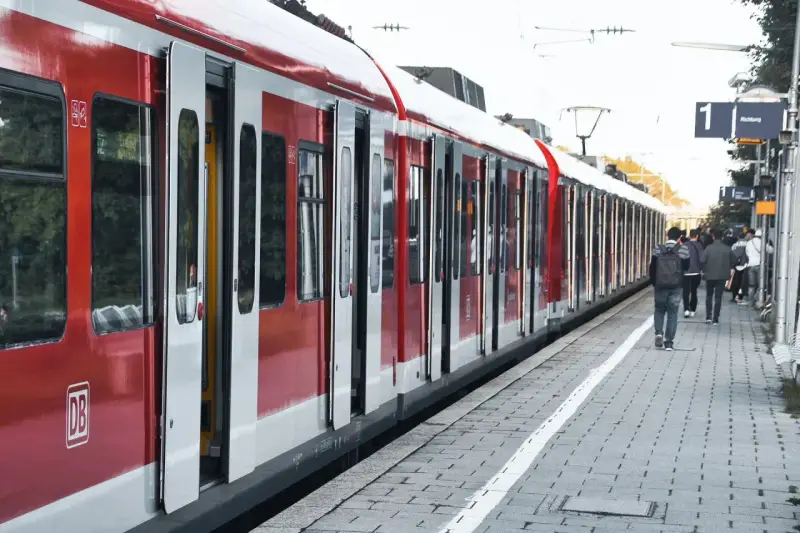 Czerwony pociąg na stacji. Ludzie czekają na peronie, zastanawiając się, jak zwrocic bilet.