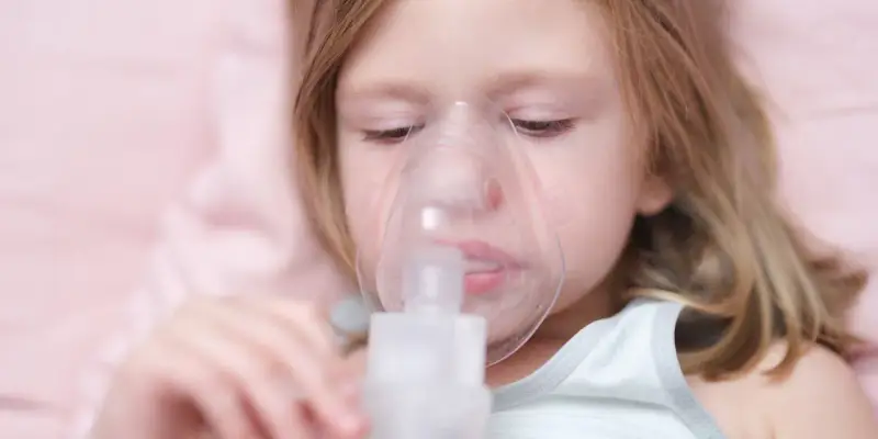 Mała dziewczynka z maską inhalacyjną na twarzy. Dziecko przechodzi inhalację na kaszel, by poczuć ulgę.