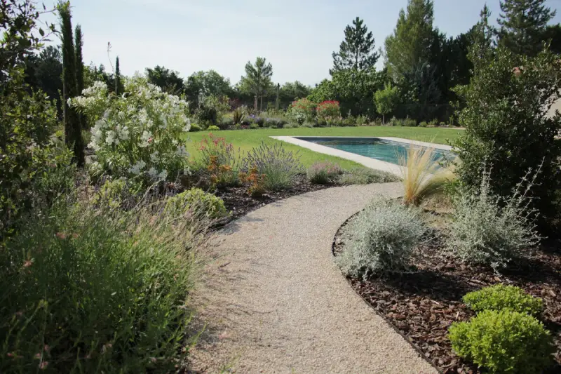 Une allée de jardin originale serpente vers une piscine, bordée de lavande, de fleurs blanches et d'arbustes verts.