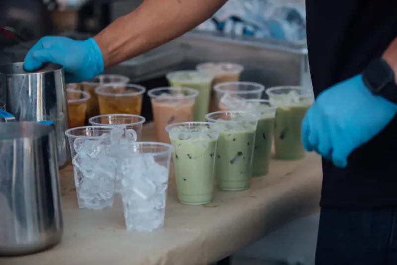 Przygotowanie do zrobienia kulek do bubble tea: ręce w niebieskich rękawiczkach, dzbanki, kubki z lodem i gotowe napoje.