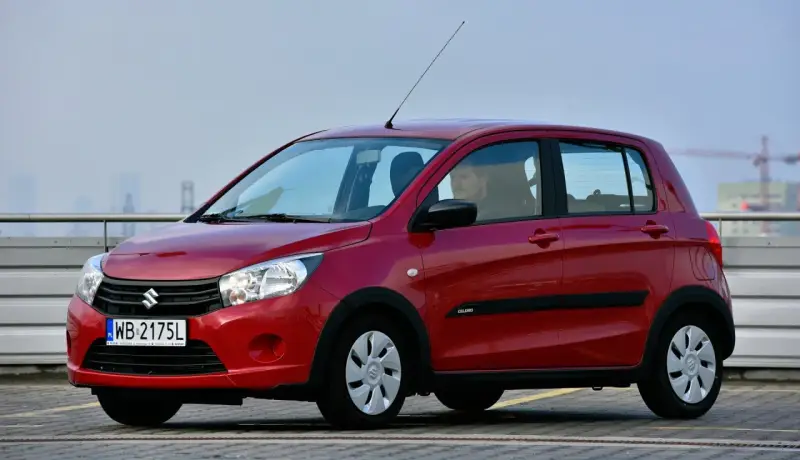 Czerwony Suzuki Celerio z polskimi tablicami rejestracyjnymi WB 2175L zaparkowany na zewnątrz.