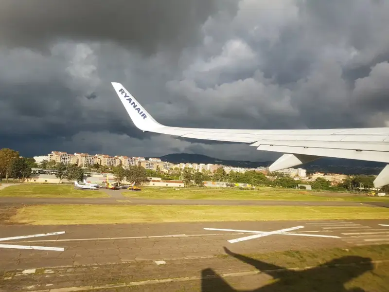 Skrzydło samolotu Ryanair nad lotniskiem, ciemne chmury na niebie.