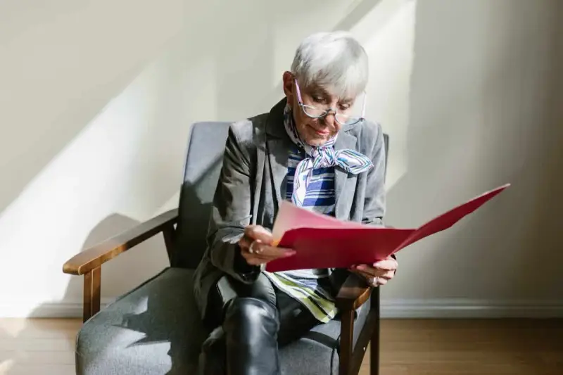 Une femme âgée, en pleine retraite, examine des documents artistiques dans un dossier rouge.
