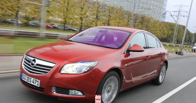 Czerwony Opel Insignia 1.6 Turbo w ruchu ulicznym. Wady tego modelu mogą dotyczyć np. spalania.