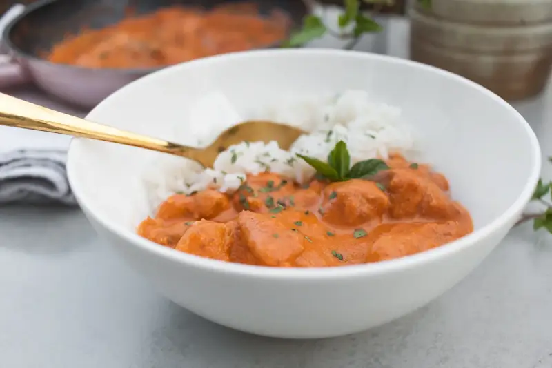 Aksamitny butter chicken masala z ryżem, udekorowany miętą. Złota łyżka zanurzona w daniu.