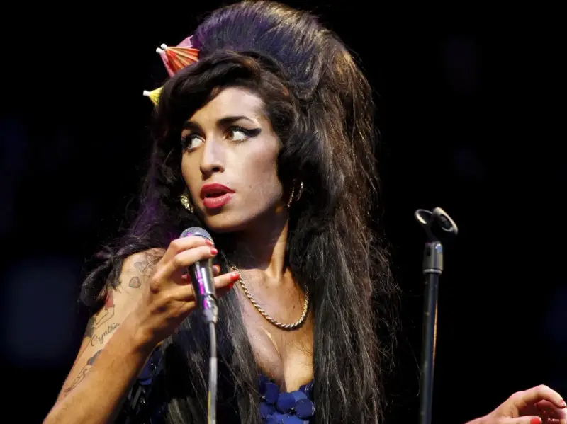 Amy Winehouse z charakterystyczną fryzurą i makijażem, śpiewająca do mikrofonu. Jej styl przypomina legendy z klubu 27, a jej muzyka wciąż żyje w sercach fanów w Polsce.
