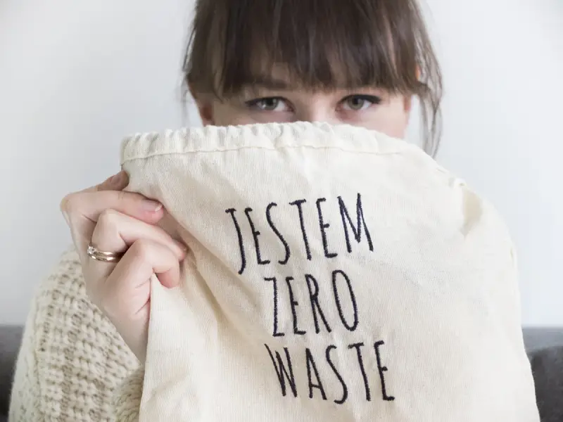 Sylwia Majcher, z uśmiechem ukrytym za torbą z napisem "Jestem Zero Waste", pokazuje swoje zaangażowanie w ekologię.