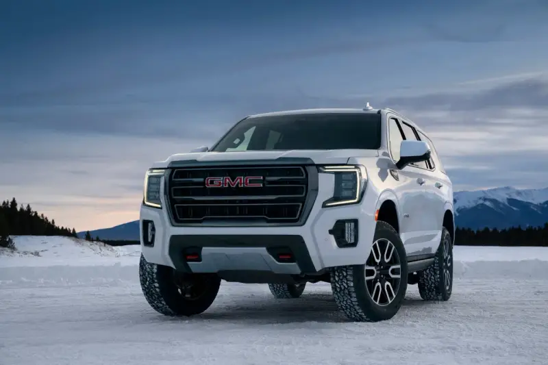 Biały GMC Yukon XL gotowy na zimową przygodę na ośnieżonej drodze, z górami w tle.
