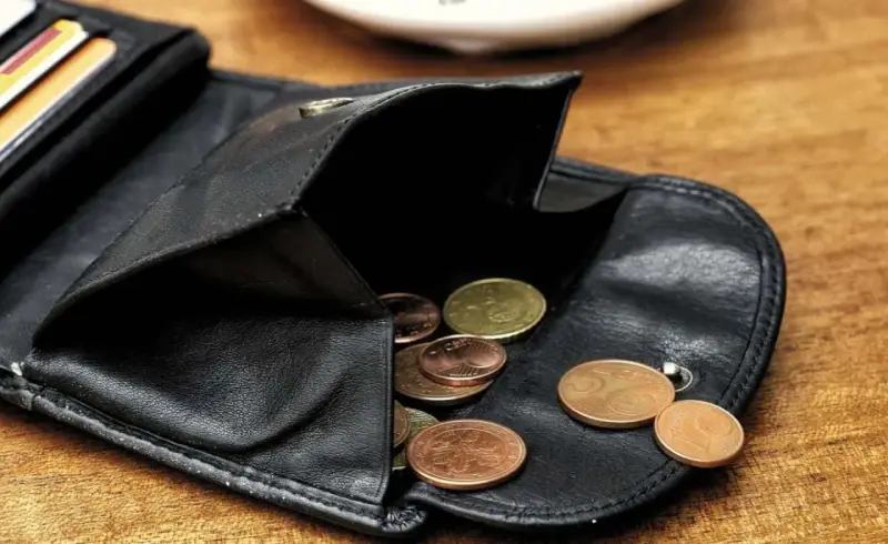 Schwarzes Lederportemonnaie mit Münzen. Die wenigen Münzen symbolisieren die Opportunitätskosten, wenn man sich für eine Ausgabe entscheidet.