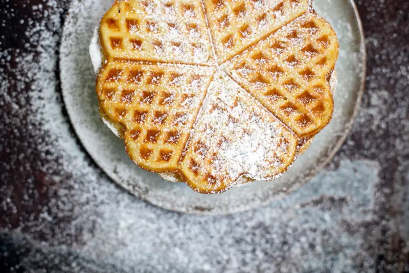 Herzförmige Waffeln, bestäubt mit Puderzucker, auf einem Teller. Ein köstliches Rezept für süße Momente.