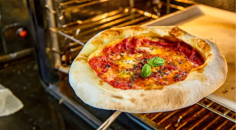 Frisch gebackene Pizza Margherita ohne Backpapier auf einem Ofenrost, mit geschmolzenem Käse und frischem Basilikum.