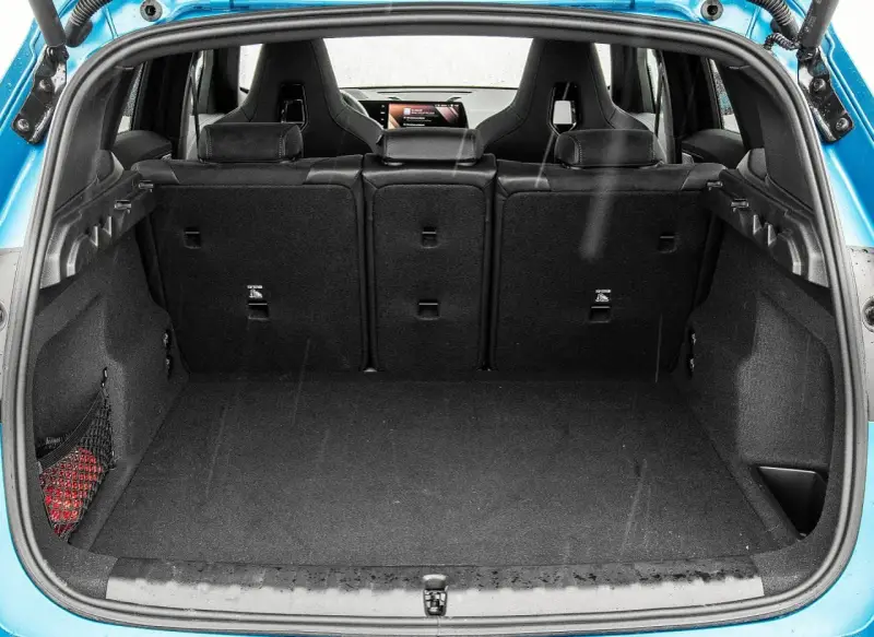 Otwarty bagażnik BMW X1, gotowy na podróż. Widoczne sportowe fotele i siatka z czerwoną gaśnicą.