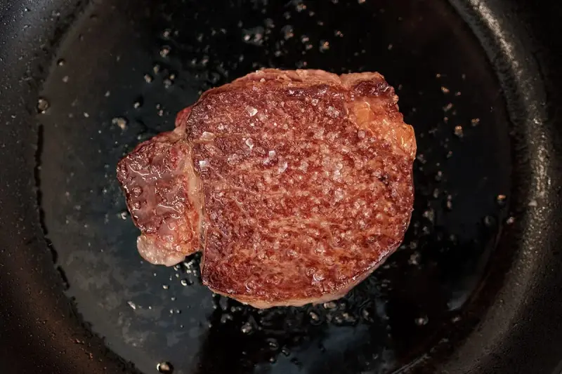 Ein saftiges Steak brutzelt in der Pfanne, bestreut mit grobem Salz.
