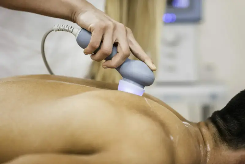 Physiotherapeutin behandelt Rückenschmerzen mit Ultraschall. Die Behandlung lindert Schmerzen nach Verletzungen.