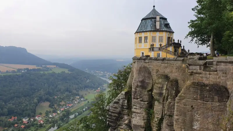 Żółty pałac na skale, część twierdzy Königstein, góruje nad doliną rzeki i lasami.