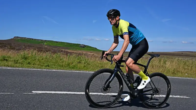 Man cycling on max speed on a scenic road with hills in the background.