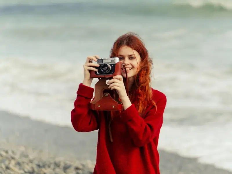 Ruda dziewczyna z aparatem, jak znani fotografowie, uwiecznia piękno morza.
