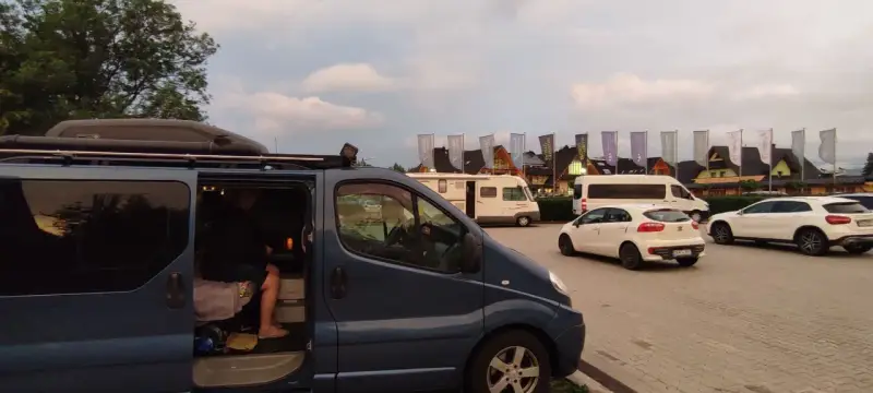 Na parkingu przy Chochołowskich Termach stoi ciemnoniebieski bus, biały samochód i kamper.