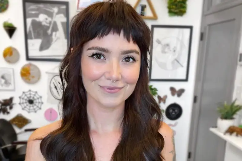 Uśmiechnięta kobieta z ciemnymi włosami i grzywką baby bangs.