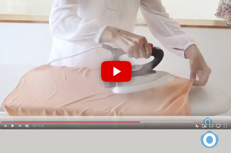 Manos planchando tela de viscosa con vapor en una tabla de planchar.