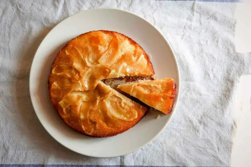 Tarta de manzana esponjosa, dorada y jugosa, con una porción recién cortada lista para disfrutar.