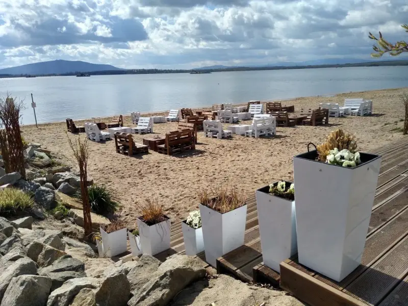 Plaża nad mietkowym zalewem z meblami z palet. W oddali góra i jezioro.