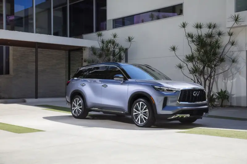 Elegancki, srebrny infiniti samochód zaparkowany przed nowoczesnym budynkiem z kamienną fasadą i dużymi oknami.