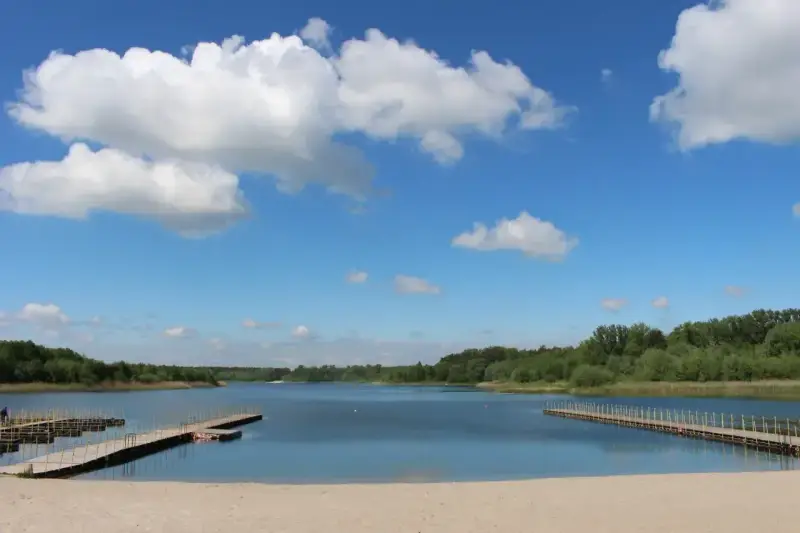 Piękny dzień nad jeziorem Wilczyńskim. Piaszczysta plaża, drewniane pomosty i błękitne niebo z białymi chmurami zapraszają do wypoczynku.