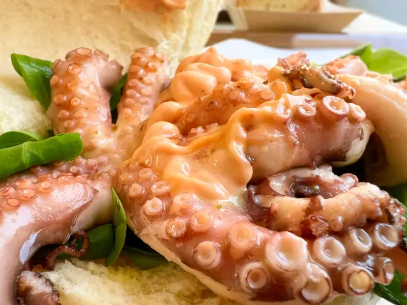 Tentacoli di polpo succulenti, un assaggio della sagra del polpo a Melendugno, serviti con pane croccante e foglie verdi.