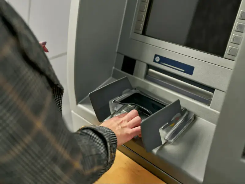 Dłoń w rękawie w kratę wkłada pieniądze do bankomatu. Szybka jednorazowa wpłata gotówki do banku.