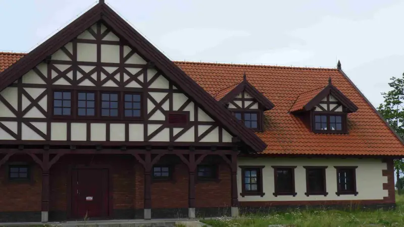 Elewacja budynku w stylu mur pruski, z charakterystyczną drewnianą szachownicą na jasnym tle i ceglanym parterem.