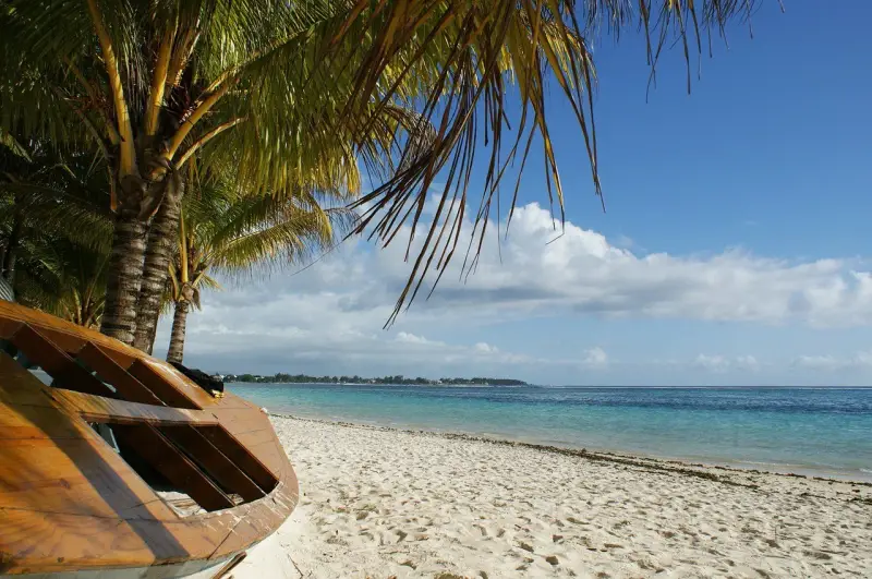 Mauritius pora deszczowa. Drewniana łódź na piaszczystej plaży pod palmami, turkusowe morze i błękitne niebo z chmurami.