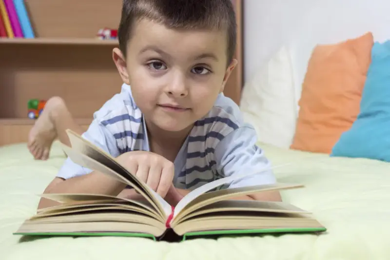 Chłopiec leży na łóżku z otwartą książką. To świetny sposób, jak zachęcić dziecko do czytania.