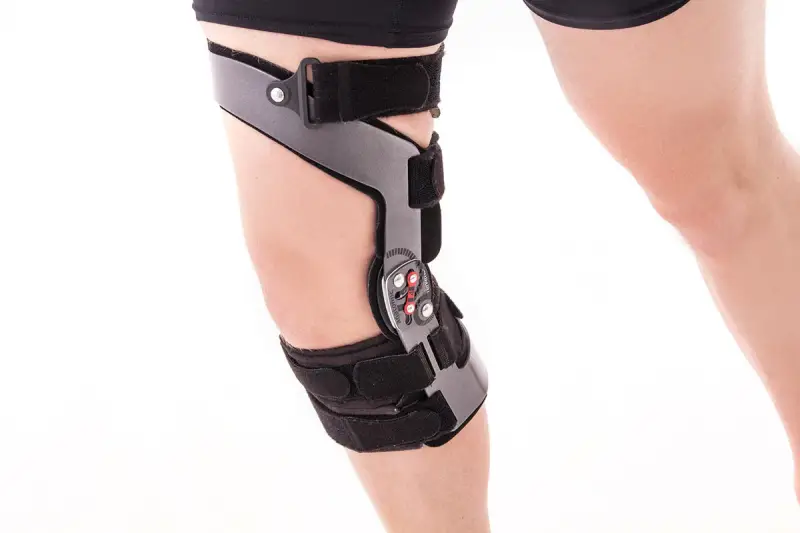 Stabilizator na kolano z metalowymi elementami i paskami na białym tle.