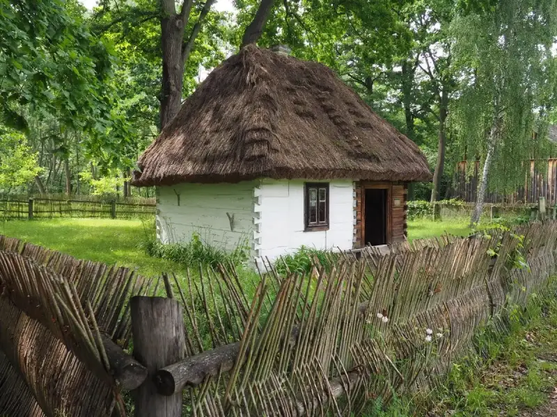 Drewniana chata z krytym strzechą dachem i płotem z gałęzi. Wspaniałe radom atrakcje, które przenoszą w przeszłość.