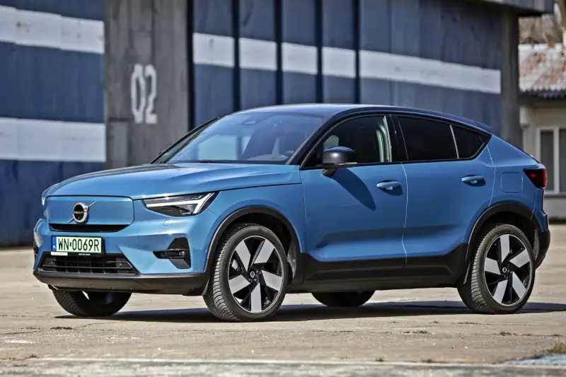 Niebieskie Volvo C40, elektryczny SUV coupe, parkuje przed budynkiem z numerem "02".