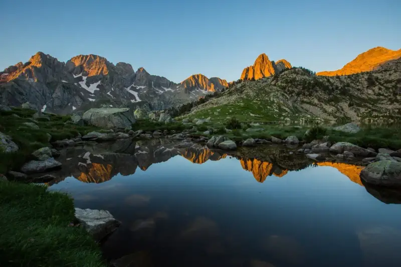 Reflejo dorado de montañas en un lago sereno del **parque natural Posets Maladeta** al amanecer.