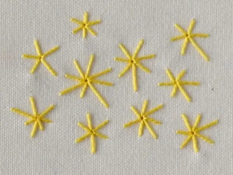 Piccole stelle gialle ricamate a punto pieno su tessuto bianco. Un esempio di come ricamare una stella a punto pieno.